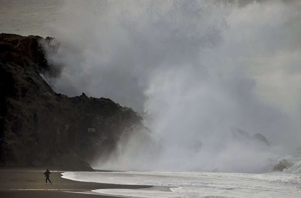 Ein Surfer (links) geht vor einer massiven Brandung an der Westküste nördlich von Bodega Bay nach einem unterseeischen Ausbruch des Vulkans Hunga Tonga Ha’apai in Tonga.