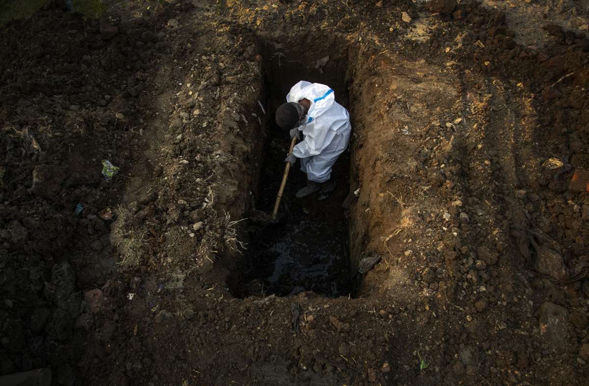 Ein Mann im Schutzanzug hebt im indischen Gauhati Erde aus, um die Leiche einer Person zu begraben, die an Covid-19 gestorben ist. Foto:  