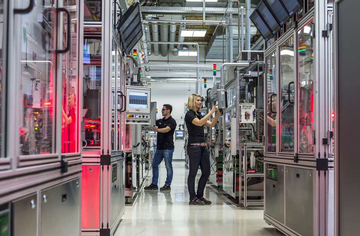 Das Bild zeigt zwei Bosch-Beschäftigte, die an Maschinen zur Herstellung von Ventilkörpern für Benzin-Direkteinspritzsysteme arbeiten. Foto: picture alliance / dpa/Daniel Maurer
