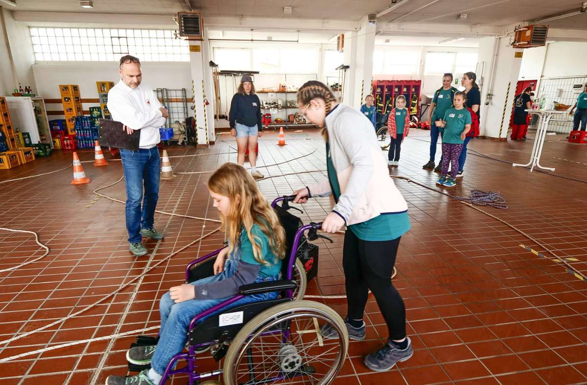 Im Feuerwehrgerätehaus ist ein Parcours aufgebaut. Ein Mensch  sitzt im Rollstuhl, der andere schiebt. Ein paar Meter weiter wird eine Hilfssituation mit „Blinden“ geprobt.