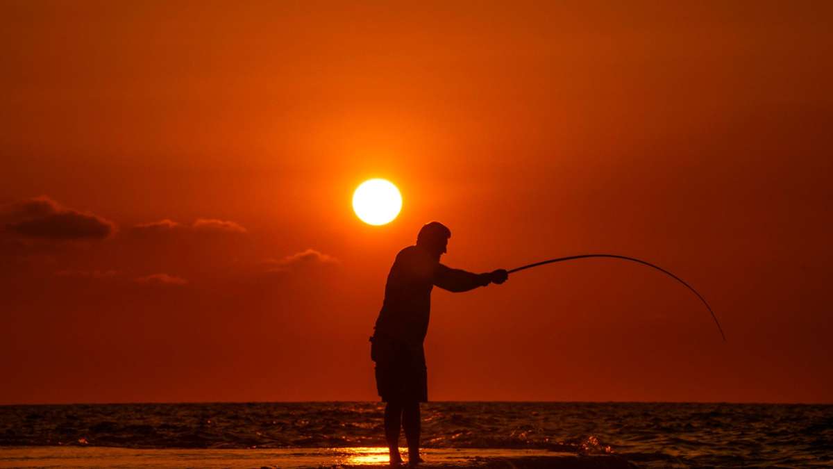 Alltag im Libanon: Ein Fischer wirft seine Angel von einem felsigen Gebiet entlang der Küste von Beirut aus, während die Sonne über dem Mittelmeer untergeht.