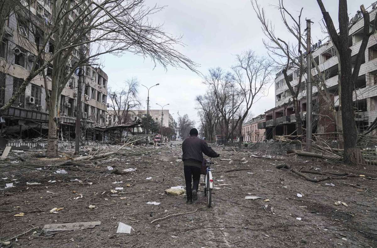 Ein junger Mann läuft mit seinem Fahrrad durch eine der zerstörten Straßen in Mariupol.