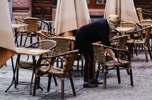 Mitarbeiterin einer Gaststätte in Heidelberg säubert auf dem Marktplatz stehende Stühle und Tische. (Archivbild) Foto: dpa/Uwe Anspach